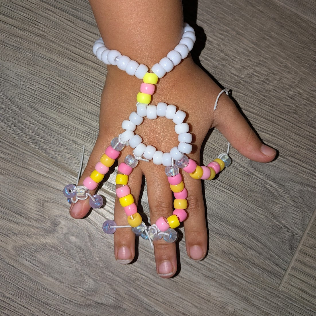 Hand wearing a colorful beaded bracelet on a wooden floor